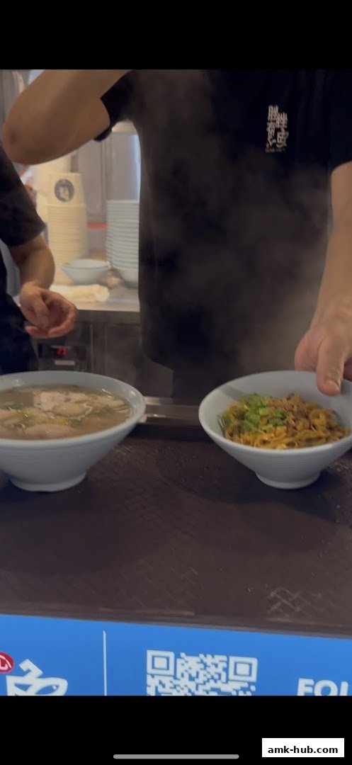 A server presents two bowls of steaming noodles, one in broth and one dry, at Cuo Cuo You Yu.