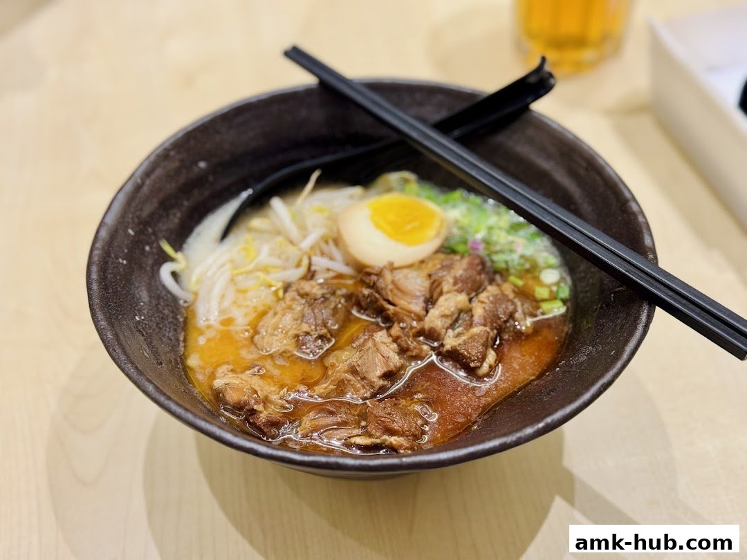 A close-up shot of a steaming bowl of ramen with tender meat, a soft-boiled egg, and bean sprouts.