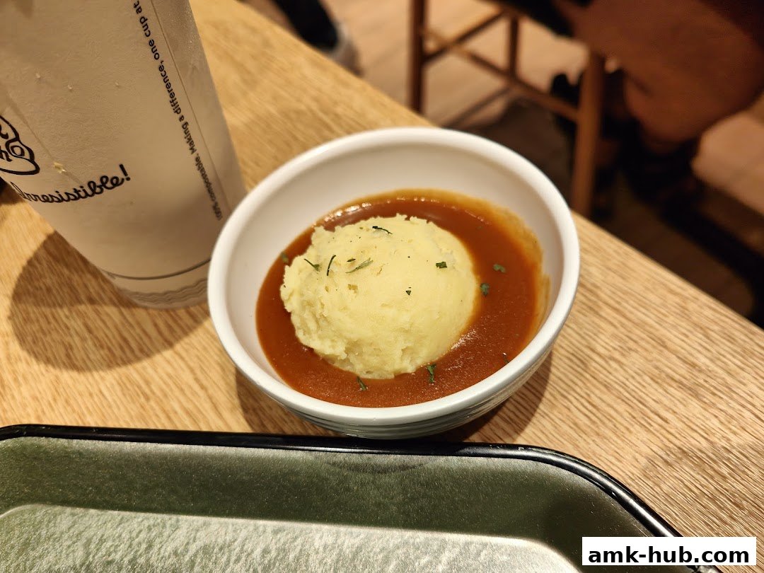 A close-up of mashed potatoes with gravy and a beverage cup on a wooden table.