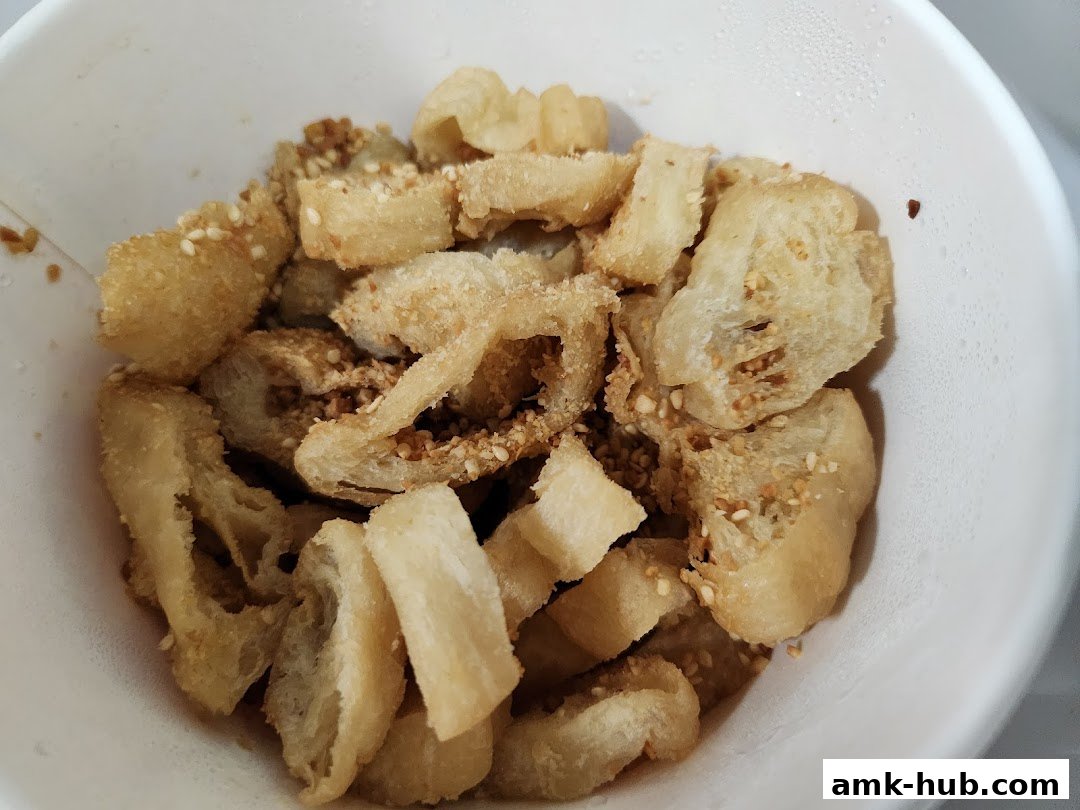 A close-up shot of crispy fried dough pieces sprinkled with sesame seeds and spices in a white bowl.
