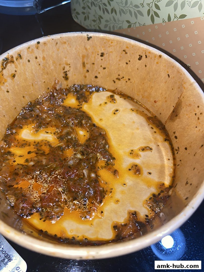 A close-up of a nearly empty takeout container with pasta sauce and herbs.