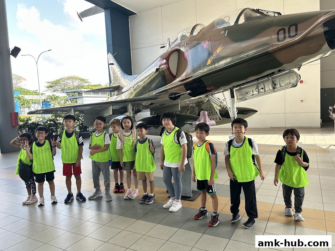Children in bright vests stand in front of a military jet aircraft.
