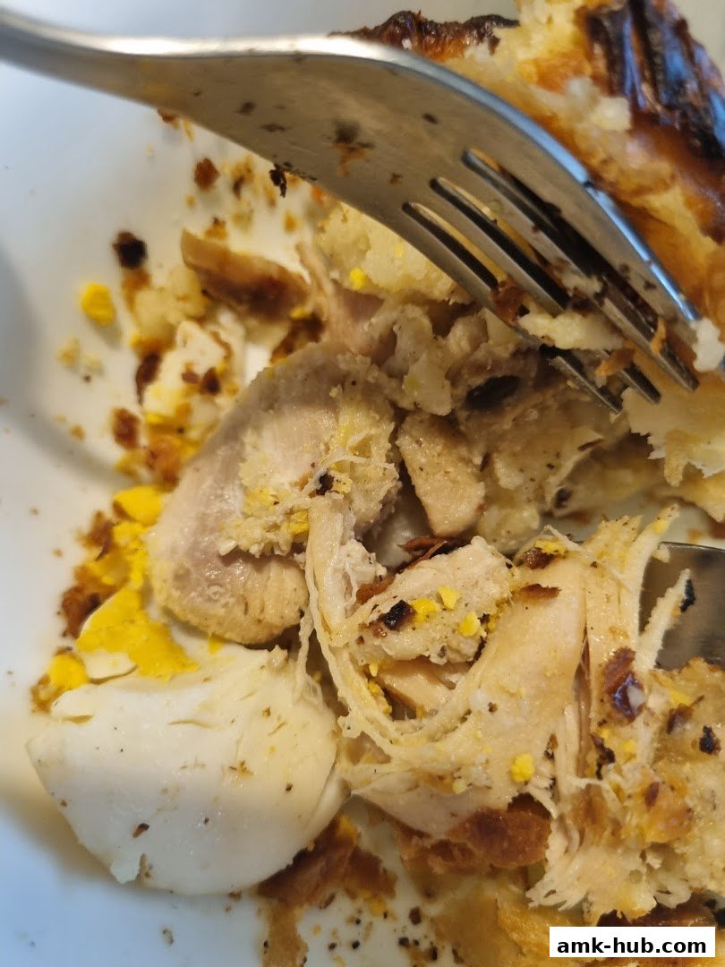 A close-up shot of a fork digging into a savory chicken pie filling with egg and pastry.