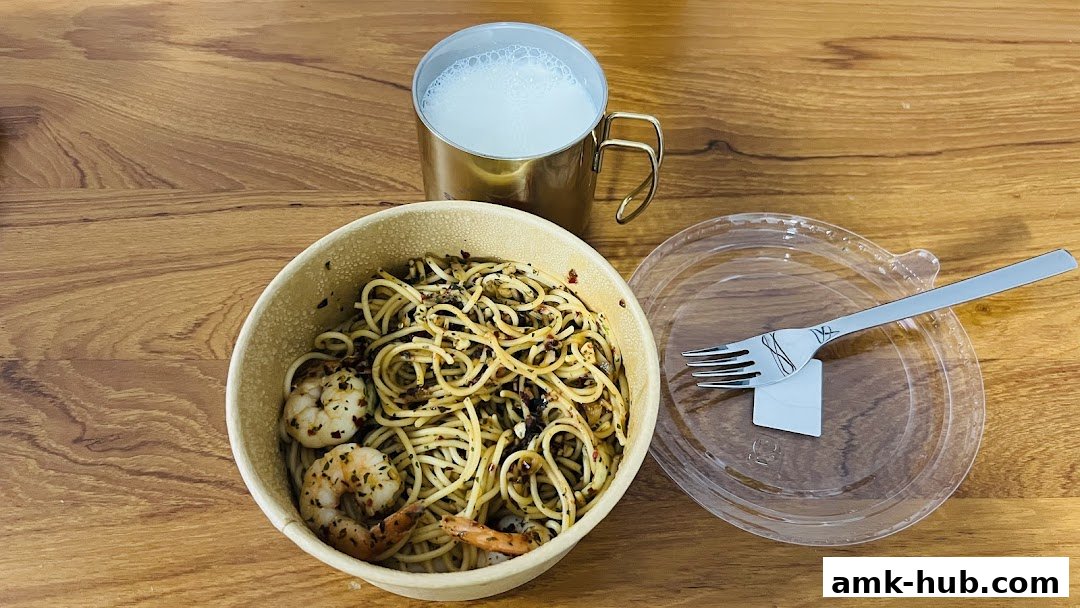 A bowl of pasta with shrimp and a drink on a wooden table.
