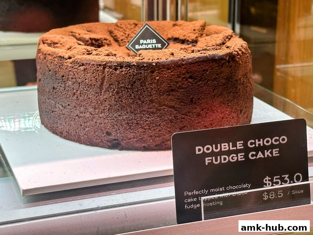 A close-up of a rich chocolate cake with cocoa powder dusting and a Paris Baguette label.