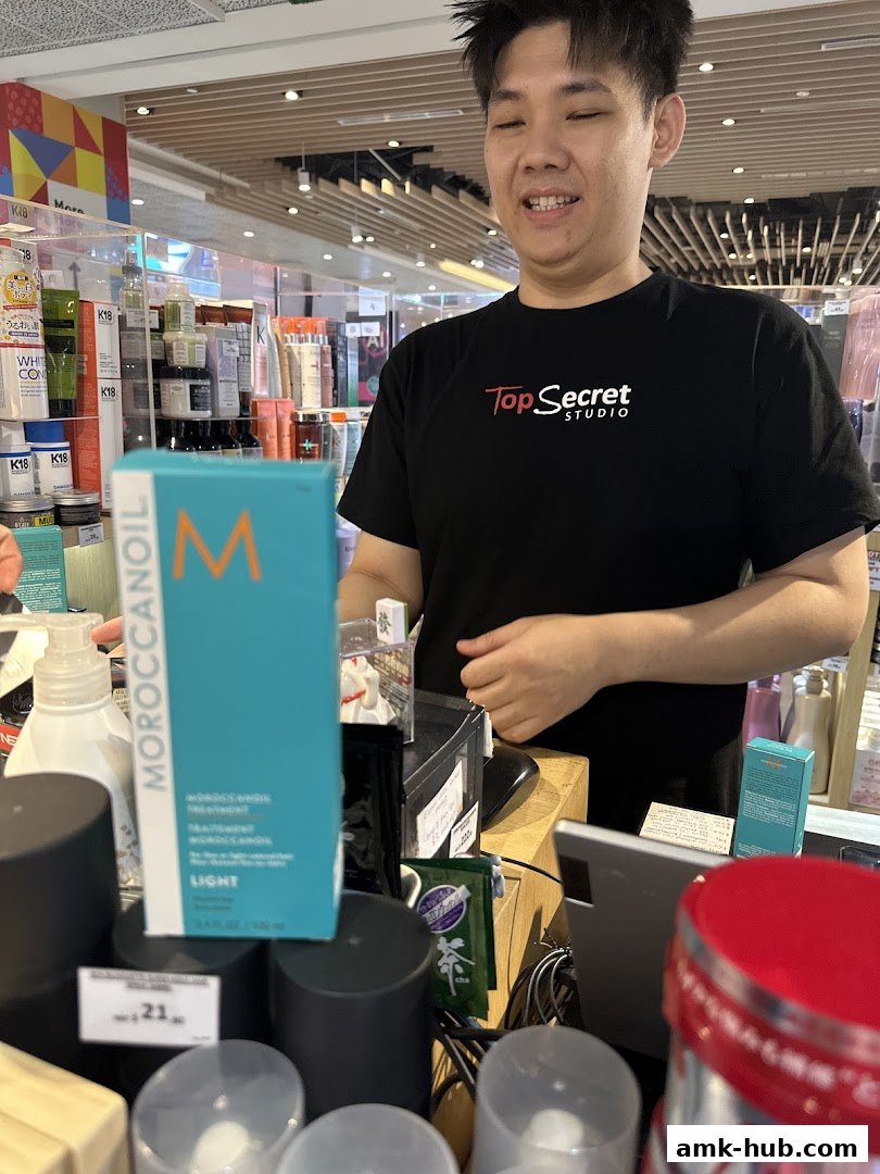 A staff member at Top Secret Studio stands behind a counter with various beauty products.