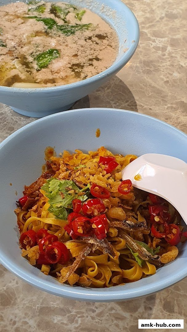 A close-up of two bowls of noodles, one dry with chili and anchovies, the other in broth.