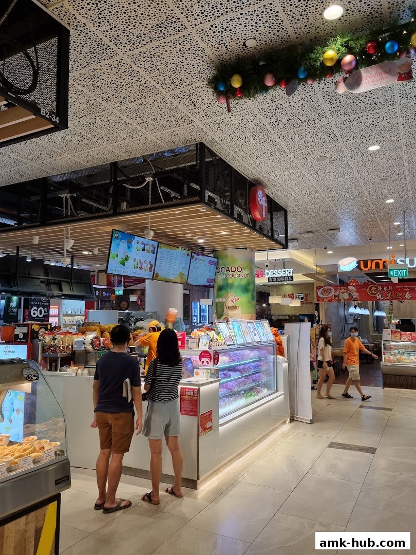 Customers at a brightly lit juice and dessert shop with a display case and digital menus.