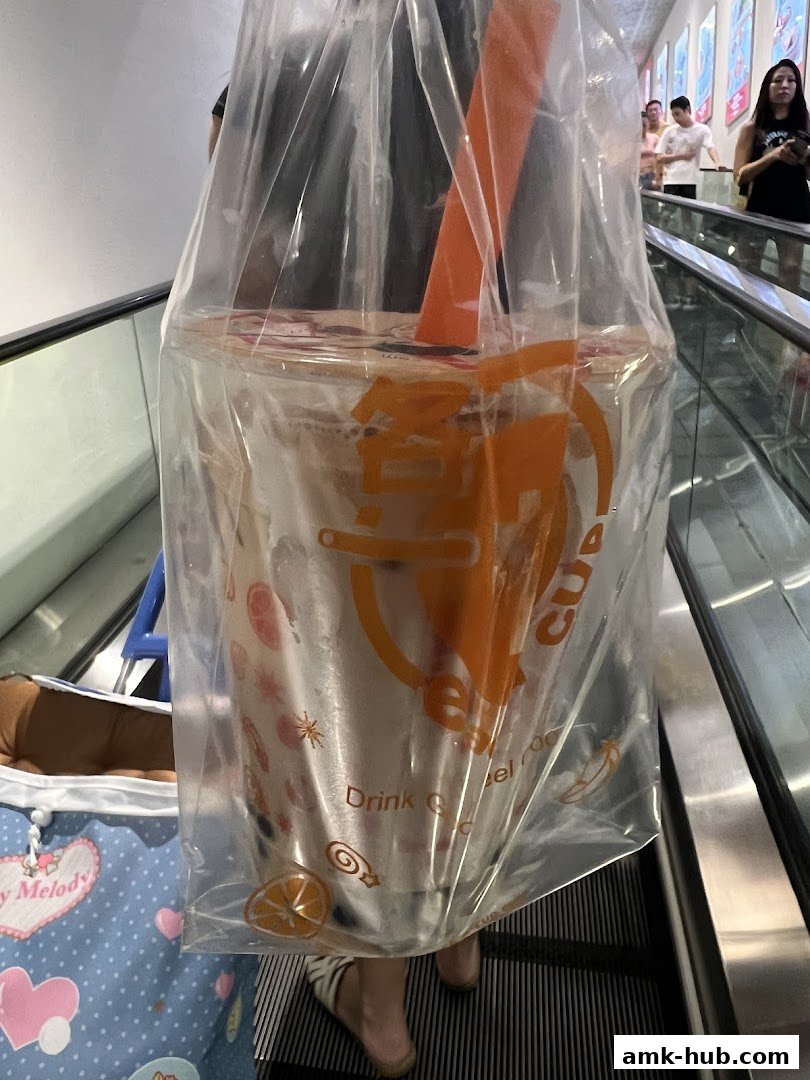 A person holds a plastic bag with a large drink from Each A Cup on an escalator.
