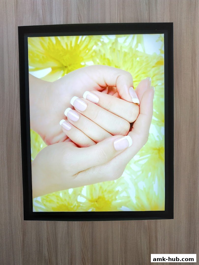 A close-up of a person's hands with perfectly manicured French tip nails against a yellow floral background.