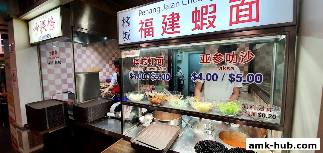 A food stall offering Penang Prawn Mee, Laksa, and Char Kway Teow with prices displayed.