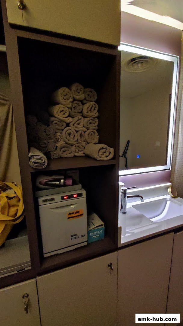 A shelf with neatly folded towels and a towel sterilizer next to a sink and mirror.