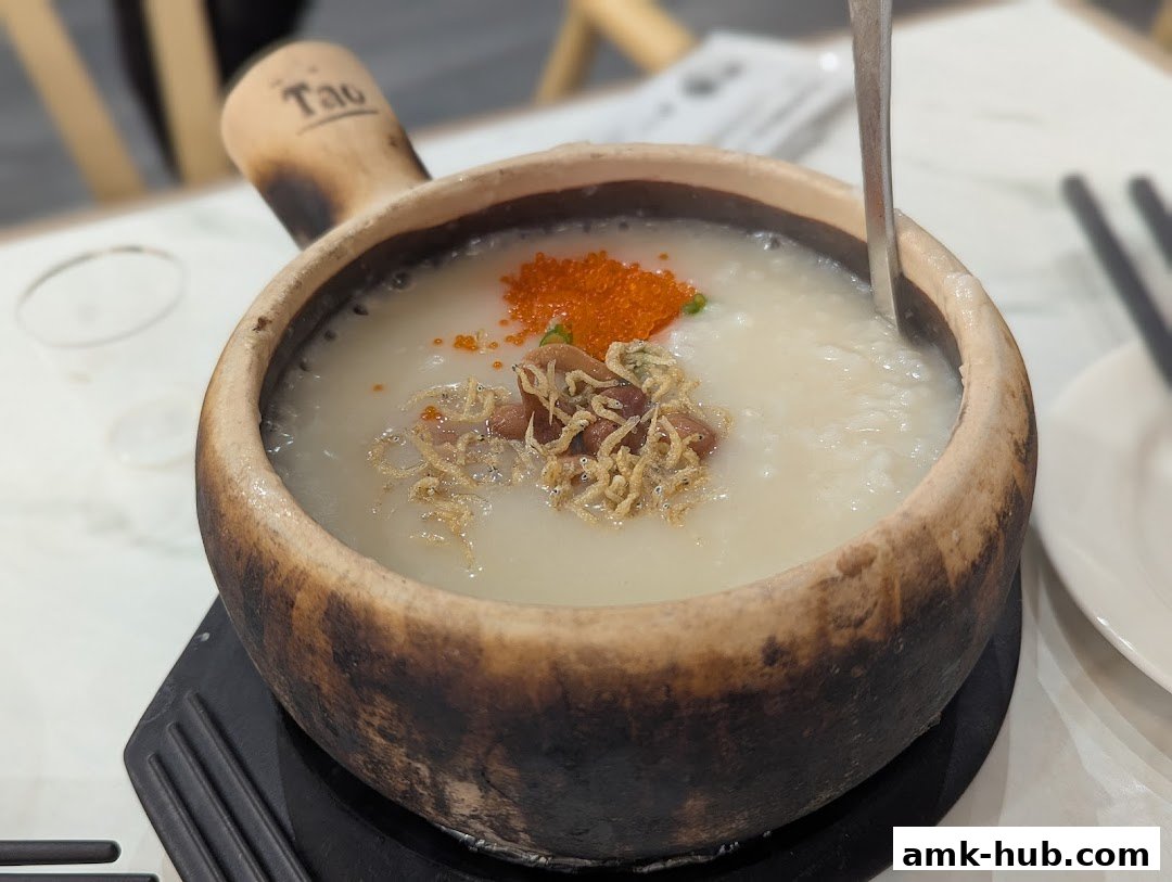 A close-up of a clay pot filled with congee, topped with fish roe and crispy anchovies.