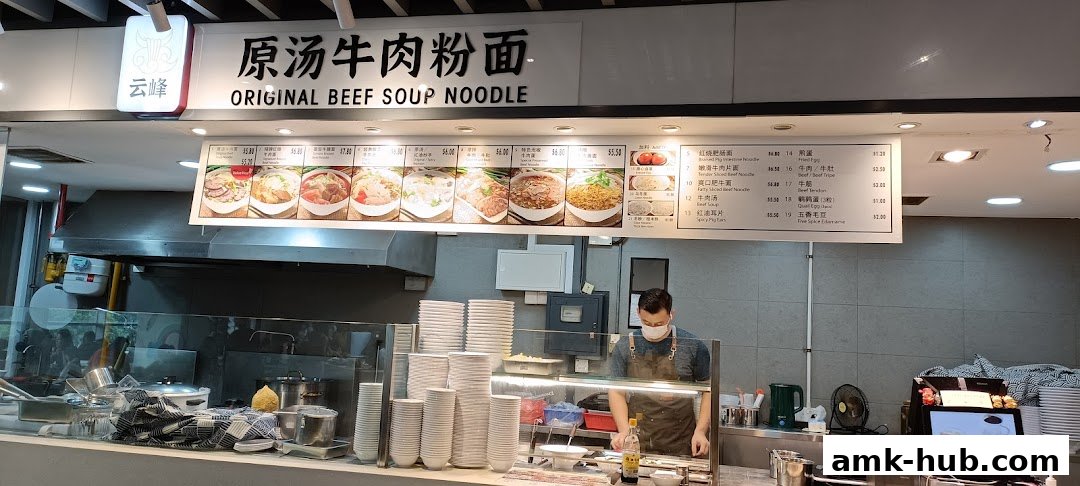A food stall counter with a menu board displaying various beef noodle dishes and other items.