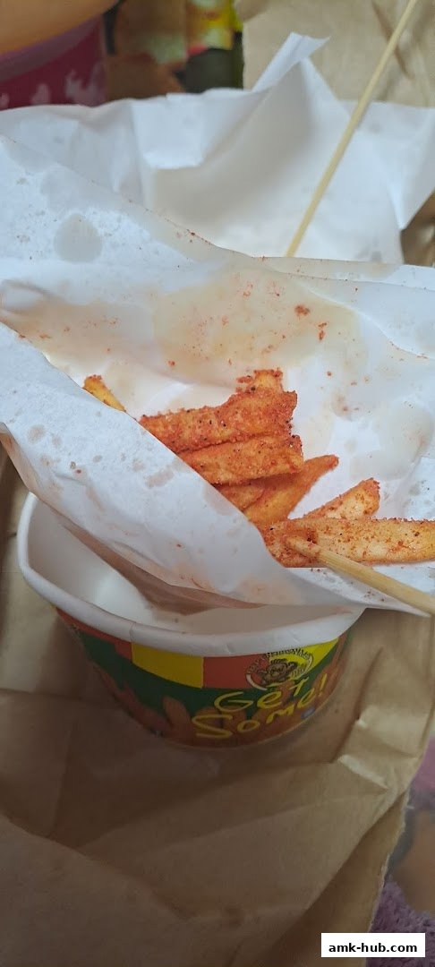 A close-up of seasoned fries served in a branded cup with a wooden skewer.