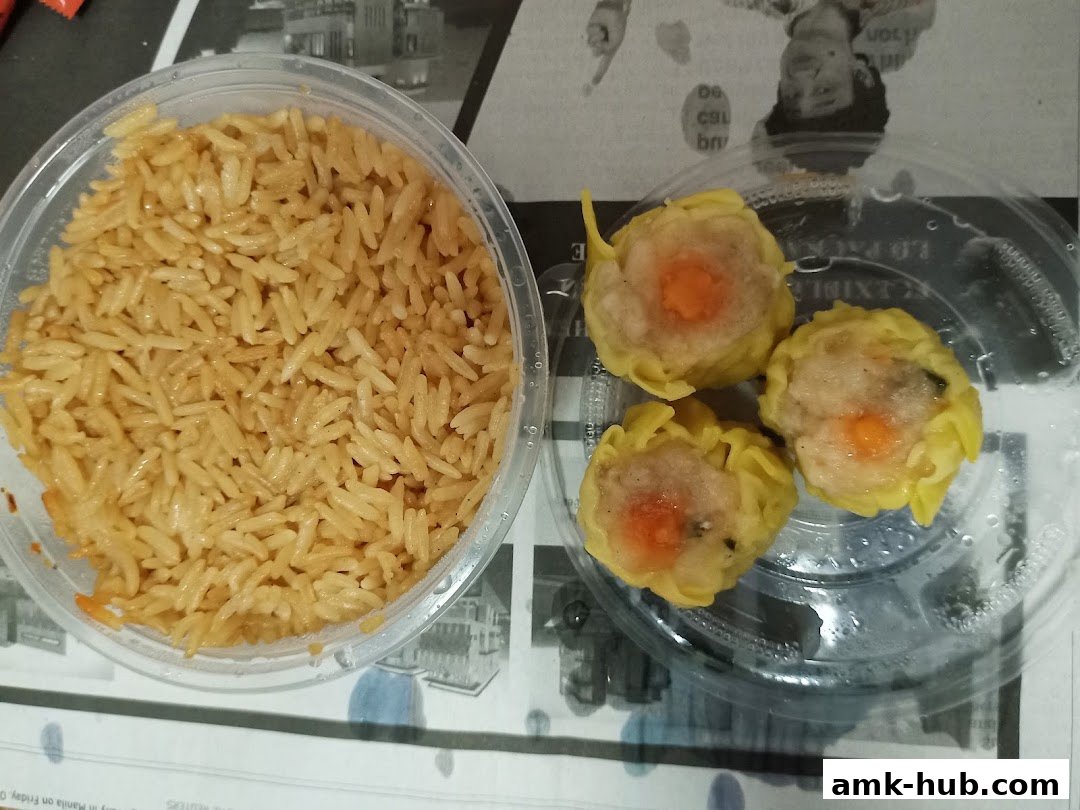 A close-up of steamed rice and three dim sum dumplings in a takeaway container.