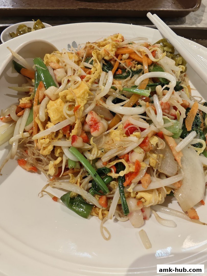 A plate of stir-fried noodles with vegetables, egg, and shrimp, served with chopsticks.