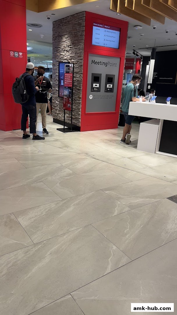 Customers interact with staff and a digital queue system at a Singtel shop.