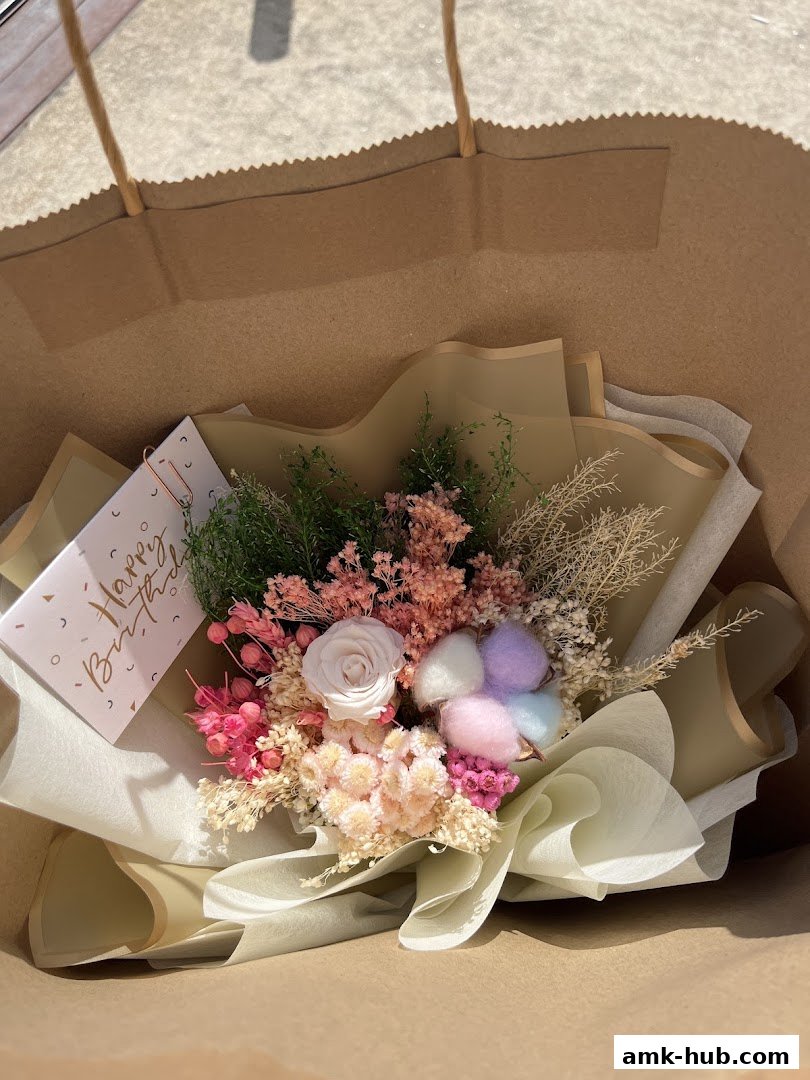 A beautiful dried flower bouquet with a 'Happy Birthday' card inside a brown paper bag.