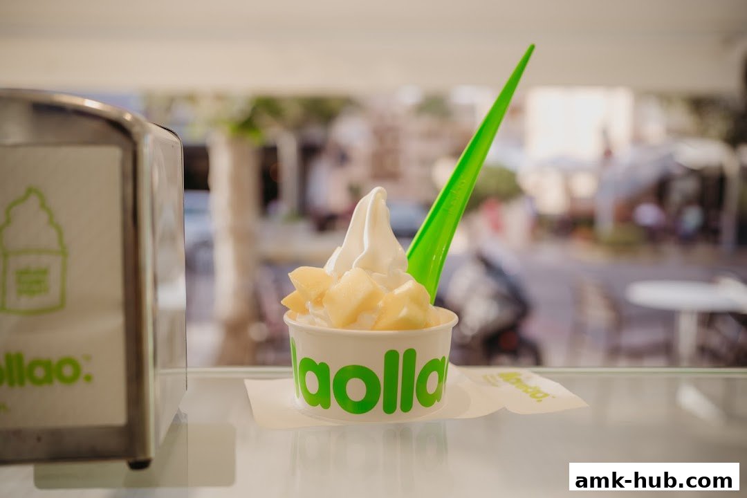 A cup of llaollao frozen yogurt with fruit toppings and a green spoon.
