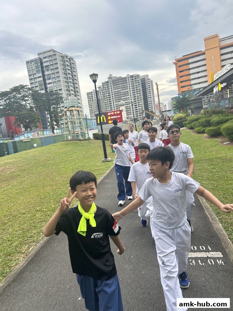 A group of children in martial arts uniforms walking outdoors, with buildings in the background.