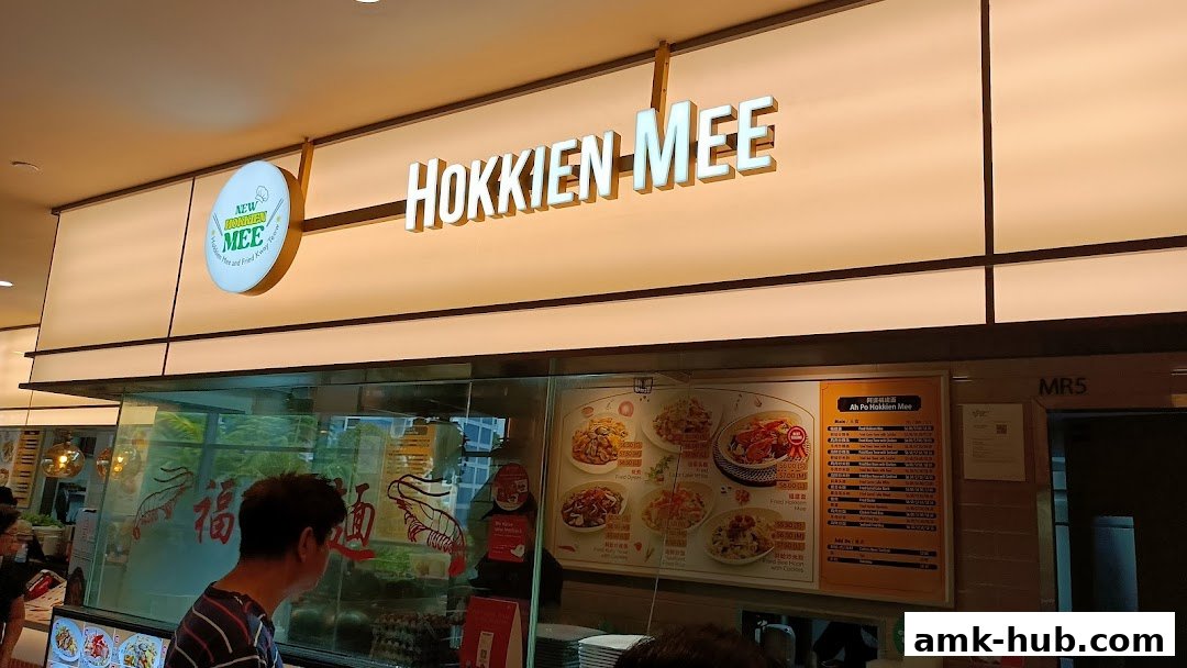 A brightly lit shop front for 'New Hokkien Mee' with a menu displayed.