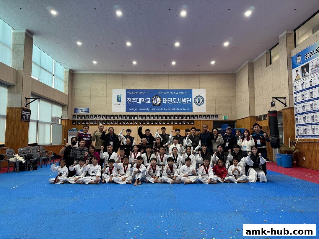 A large group of people, mostly young students in Taekwondo uniforms, pose for a photo in a gymnasium.