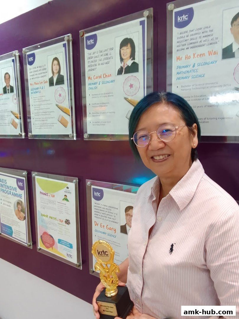 A woman proudly holds a trophy in front of a wall displaying tutor profiles and course information.