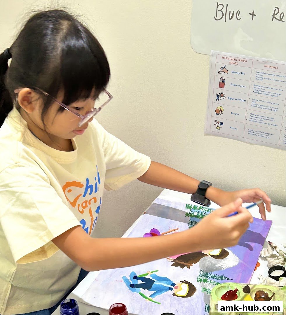 A young girl with glasses paints at a table, focused on her artwork.