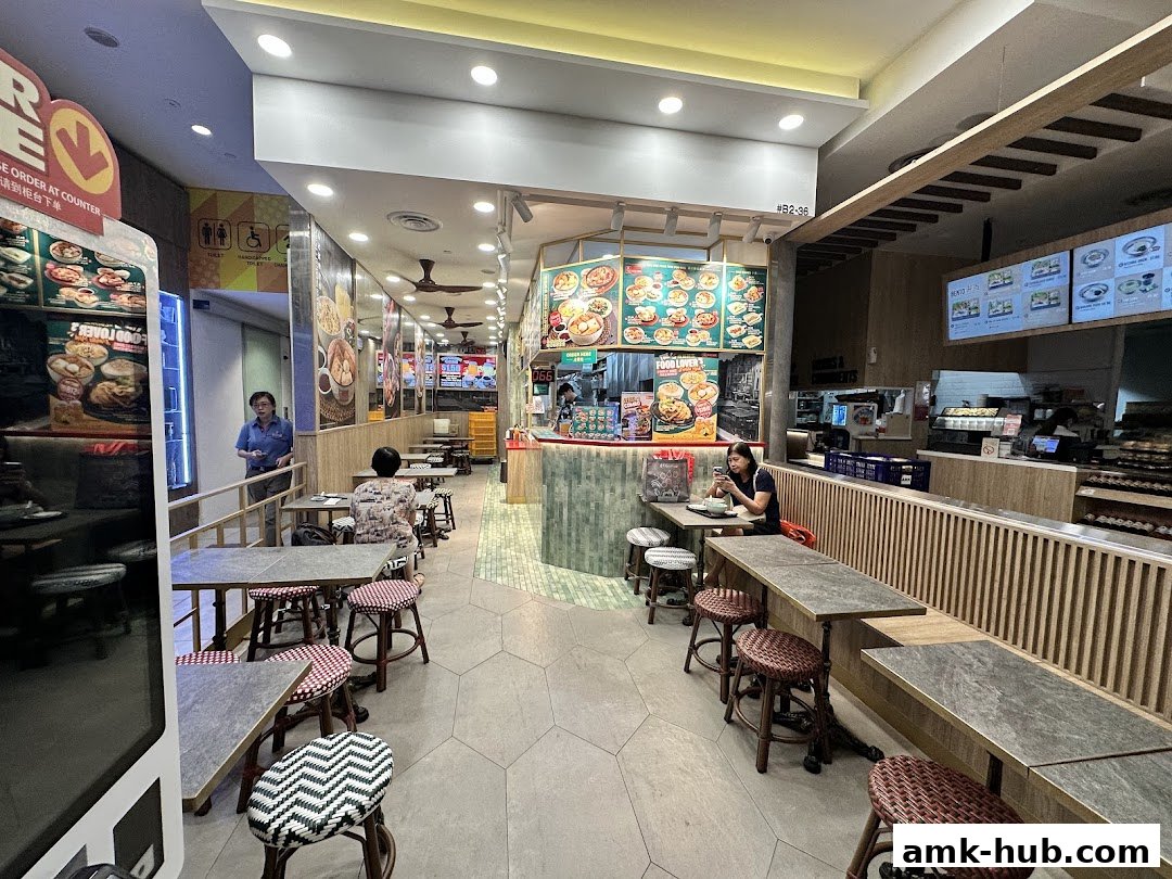Interior view of a Koo Kee restaurant with customers seated at tables and a counter.