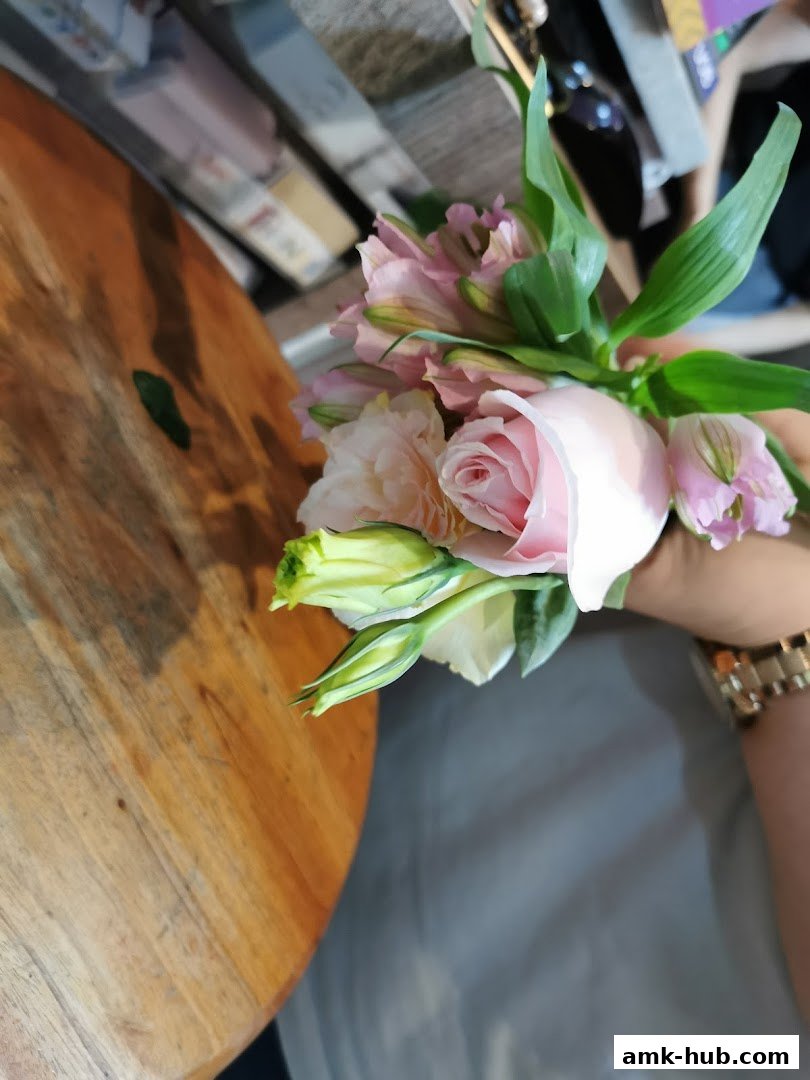 A hand holding a bouquet of pink roses and other flowers with green leaves.