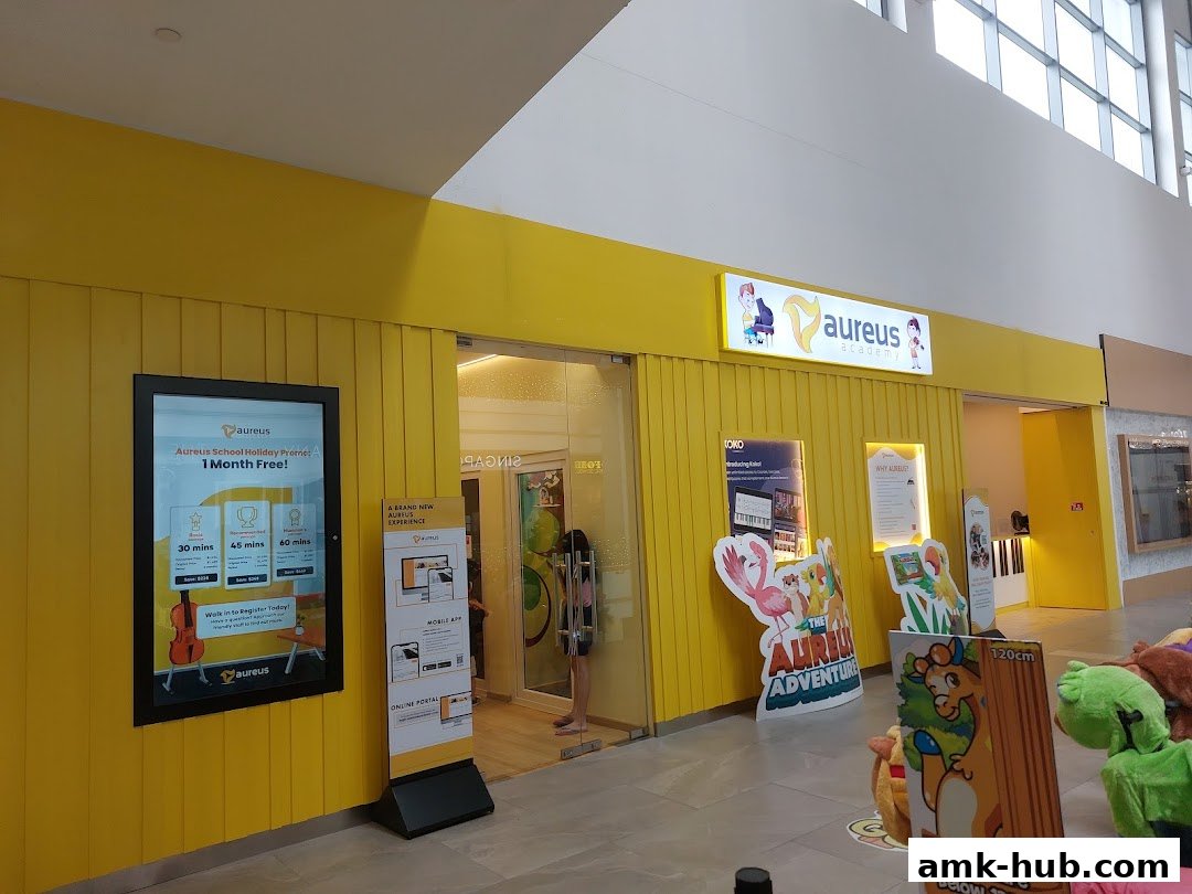 The bright yellow storefront of Aureus Academy, featuring a digital display and promotional posters.