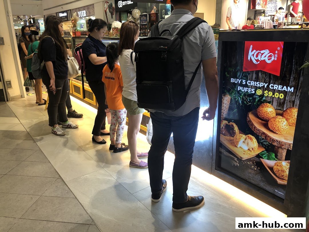 People queuing at a Kazo shop with a promotional display for crispy cream puffs.