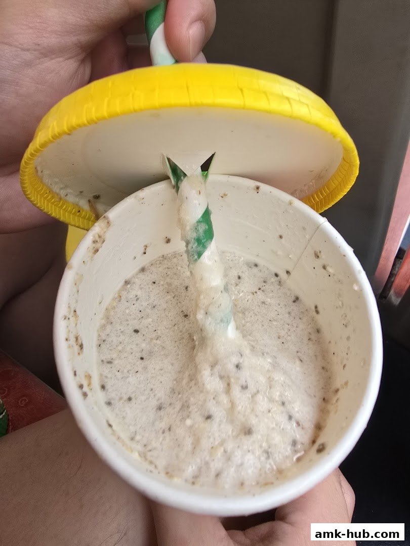 A close-up of a creamy beverage with a straw in a white cup with a yellow lid.