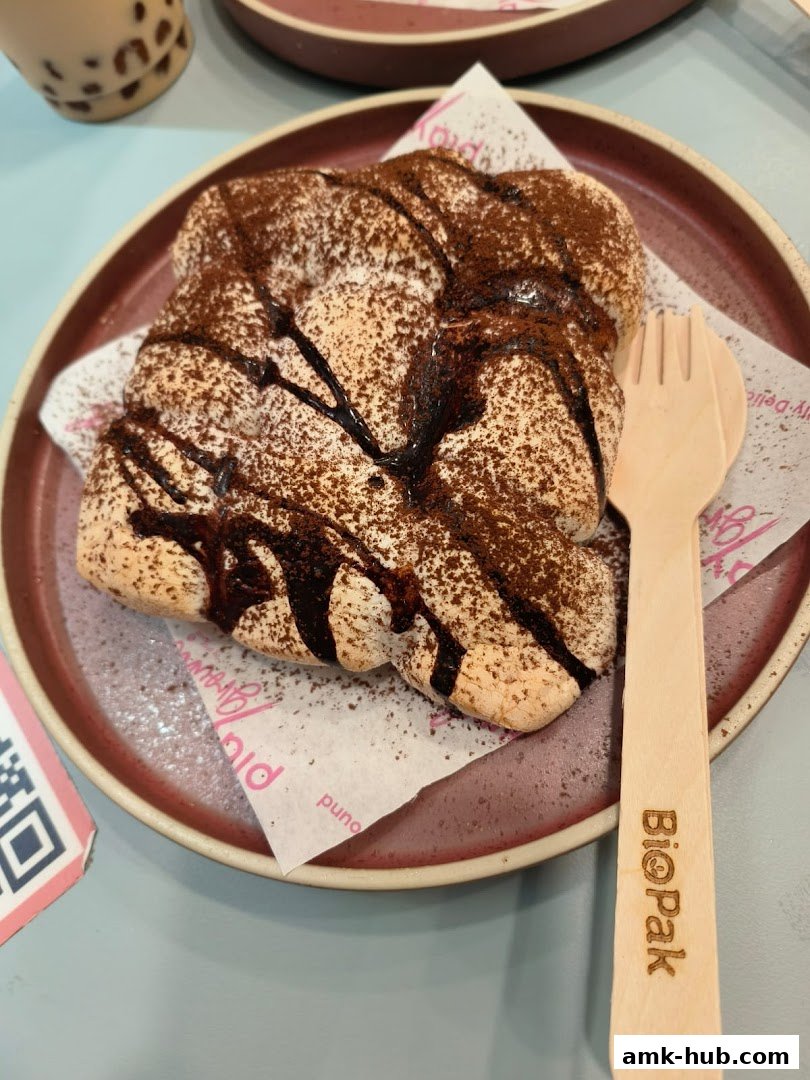 A close-up of a dessert topped with cocoa powder and chocolate drizzle, served with a wooden fork.
