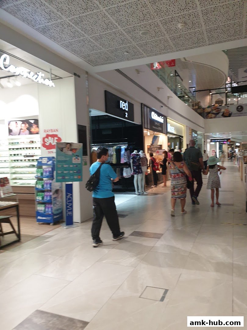 People walking in a mall hallway past various shop fronts, including Red 2.