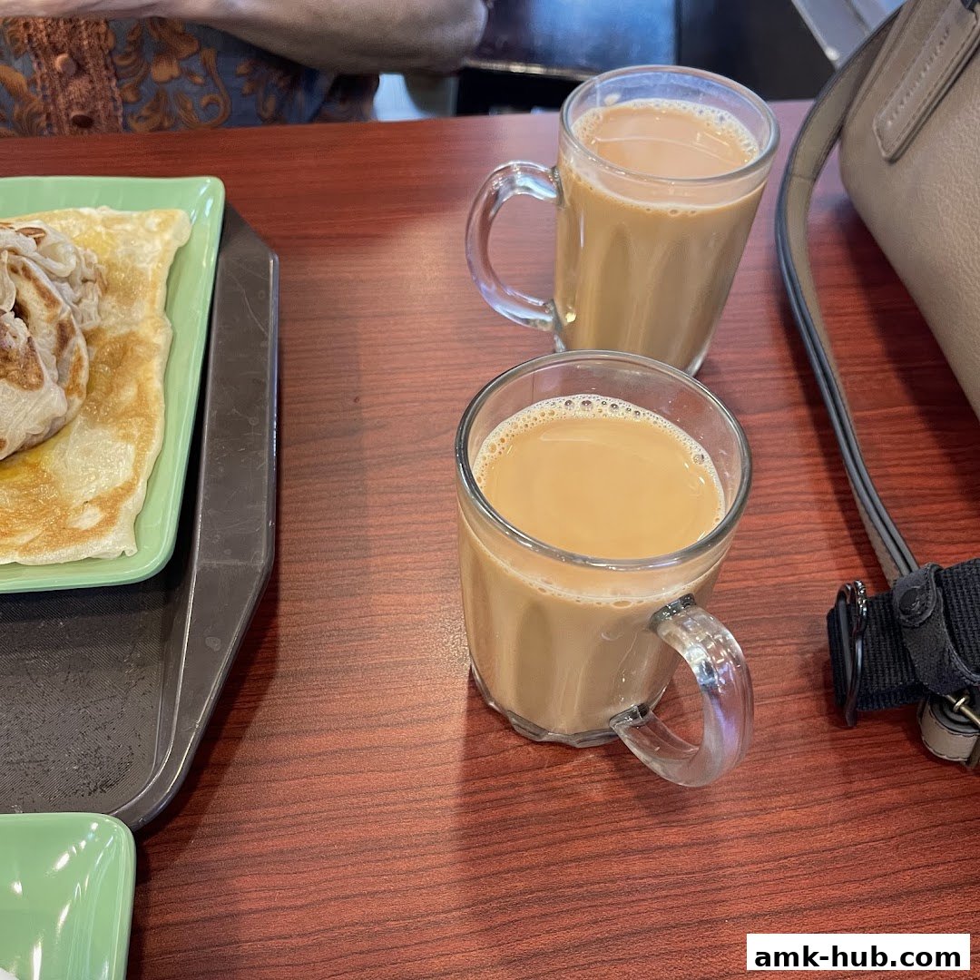 Two glasses of milk tea and a plate of roti canai on a wooden table.