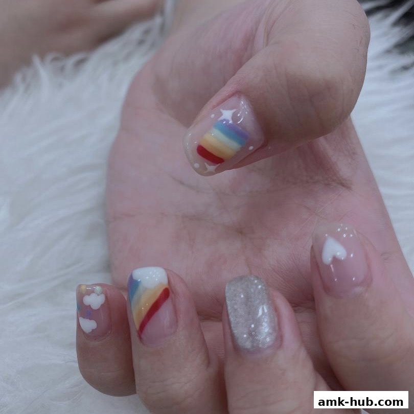 A close-up of a hand with colorful rainbow and cloud nail art designs.