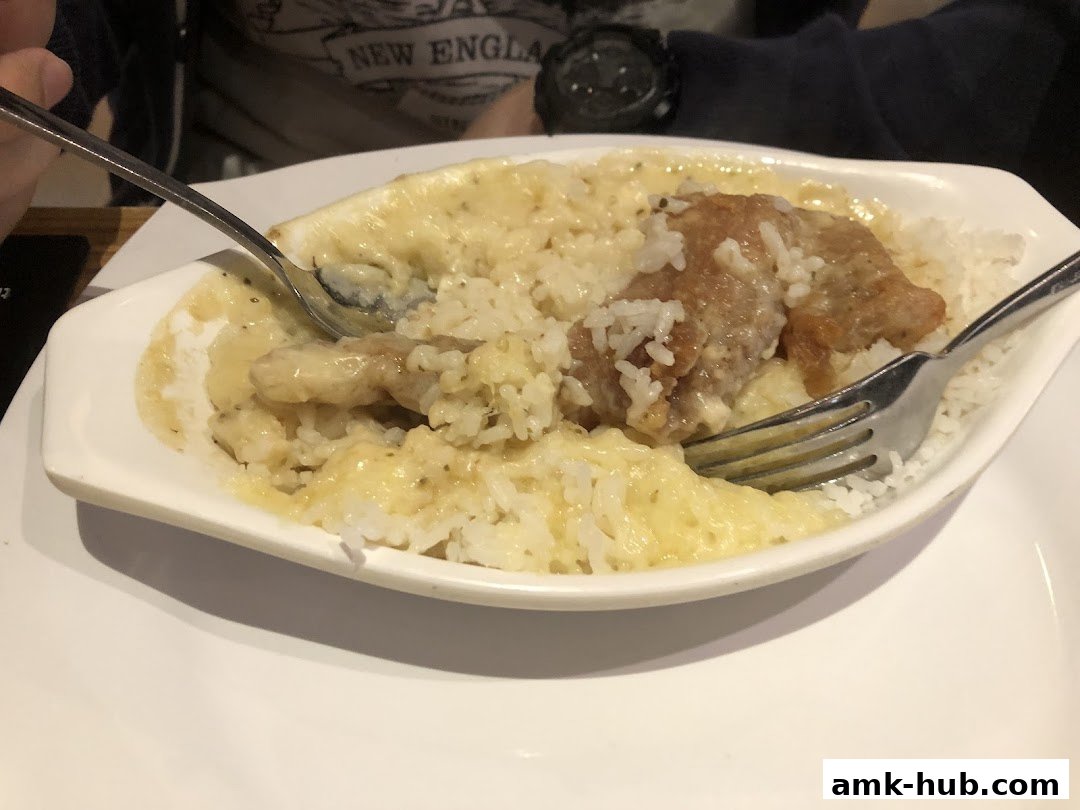 A close-up shot of a creamy chicken and rice dish being eaten with a fork and spoon.