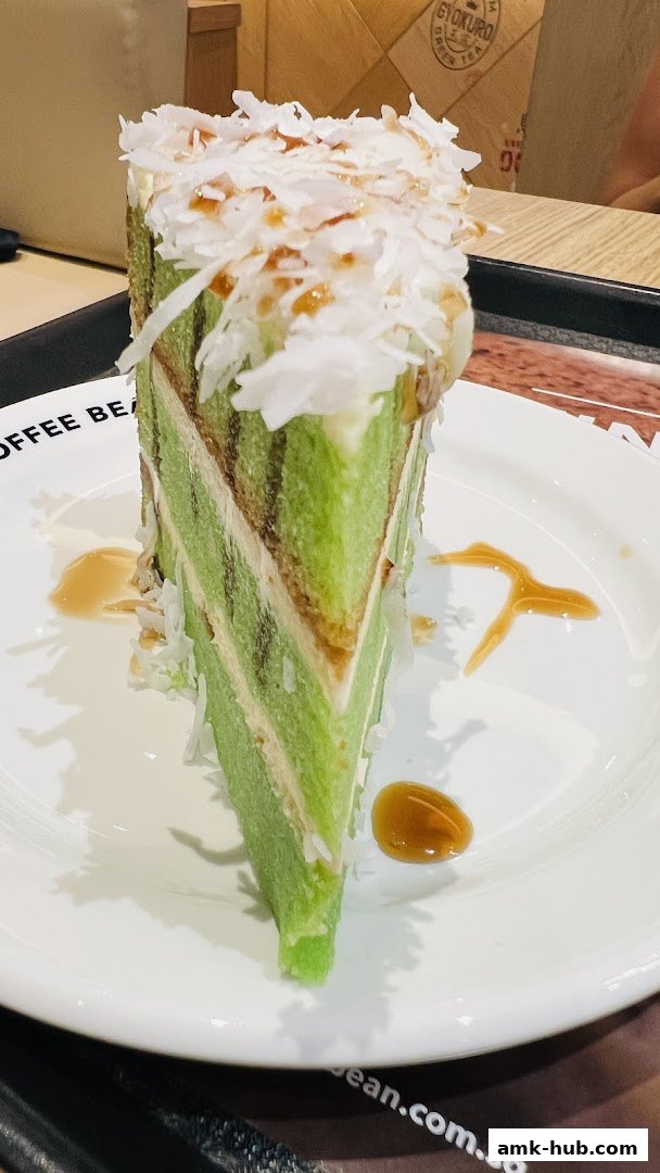 A slice of layered green cake topped with shredded coconut and drizzled with caramel sauce.