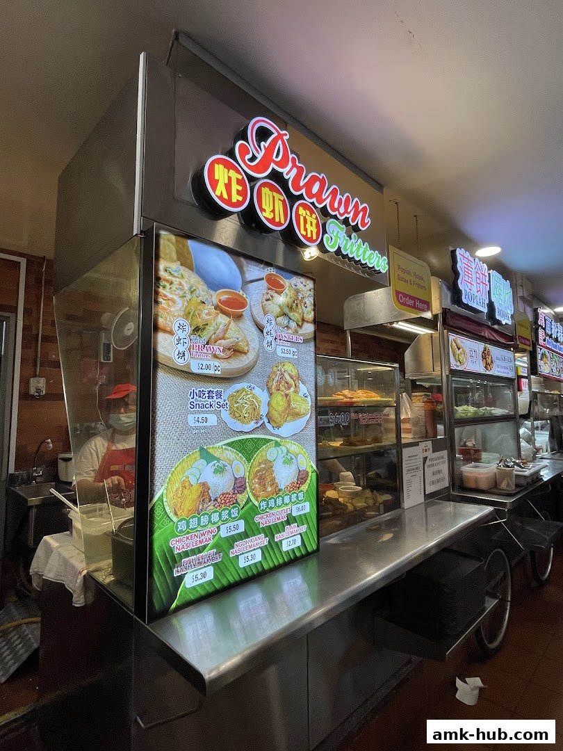 A food stall with a bright sign advertising 'Prawn Fritters' and various meal sets.
