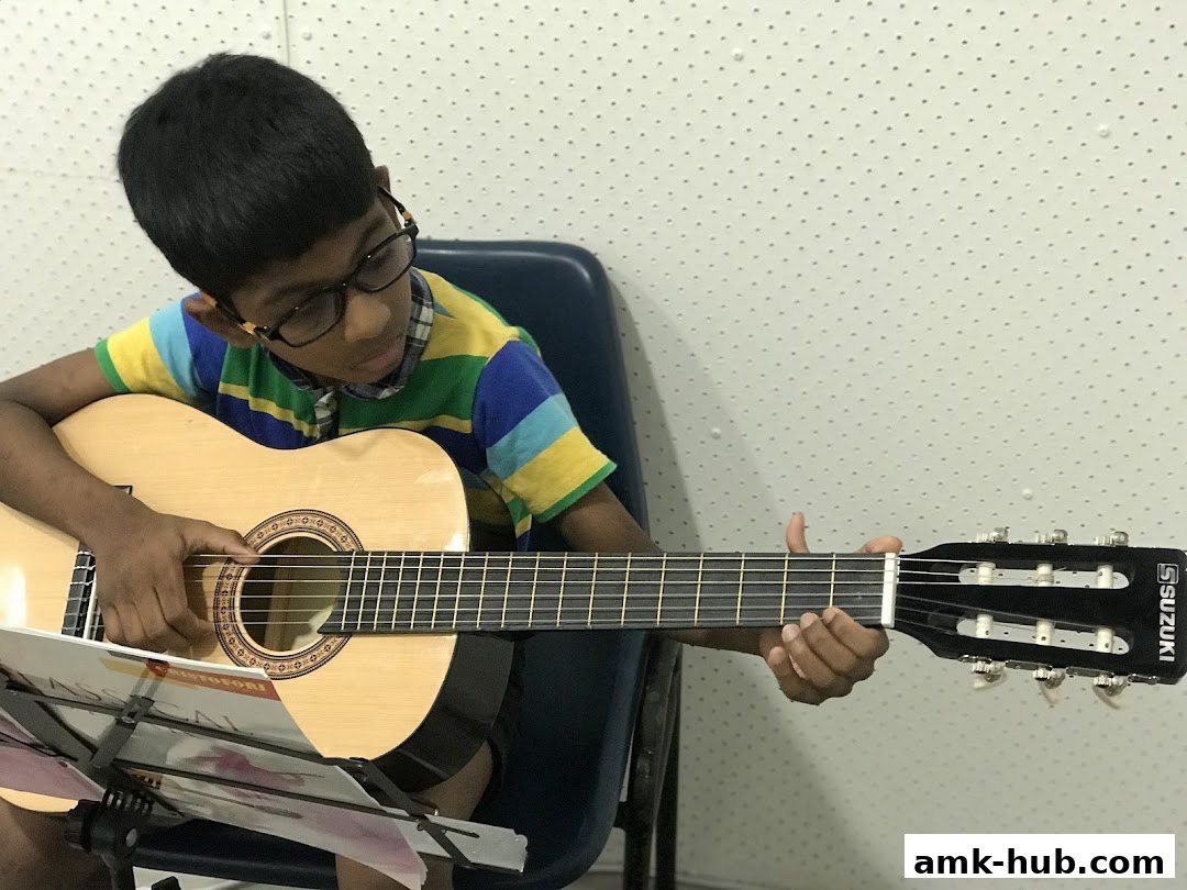 A young boy with glasses plays an acoustic guitar, focused on learning.