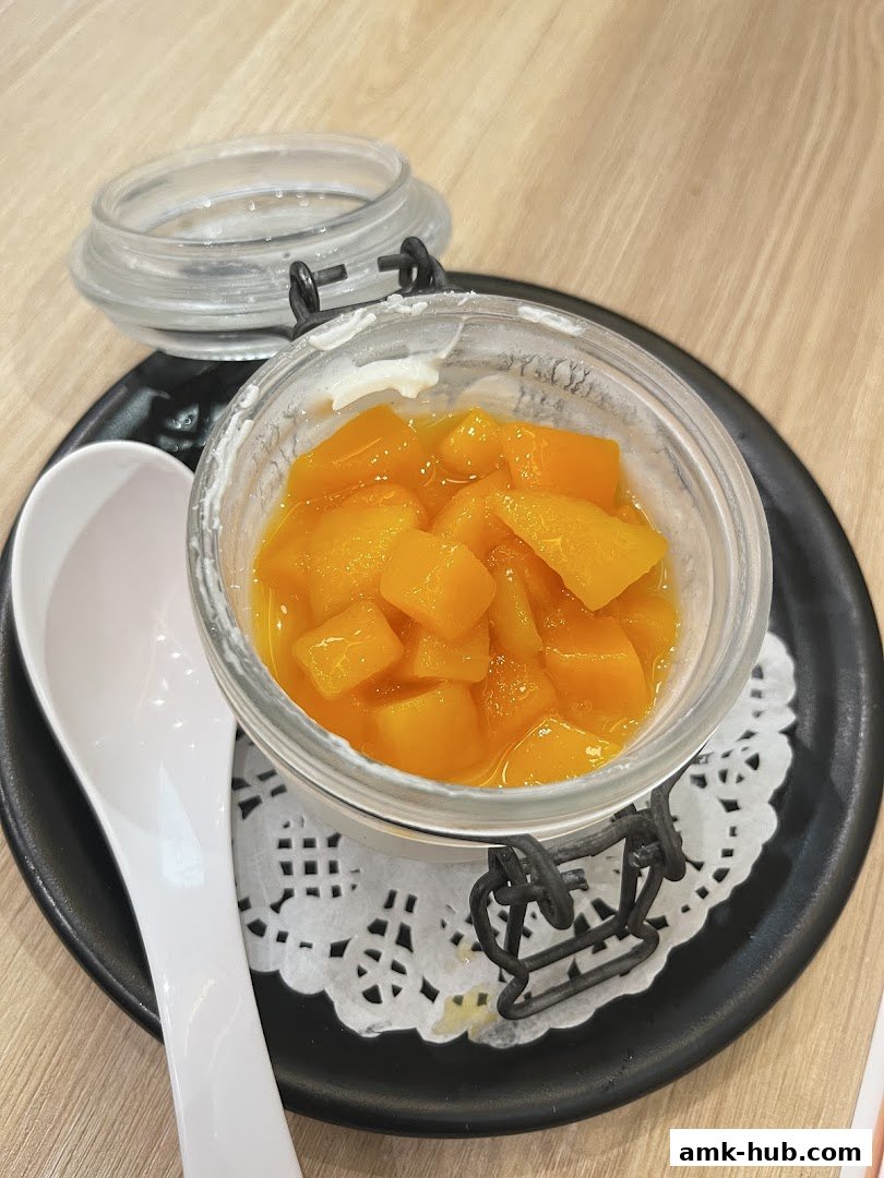 A close-up of a dessert in a jar with diced mango and a spoon.