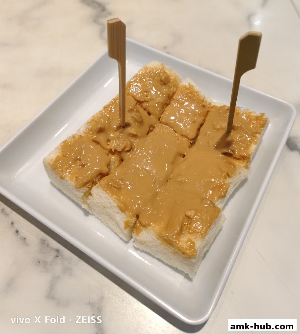A white plate holds sliced toast generously spread with peanut butter, garnished with wooden skewers.