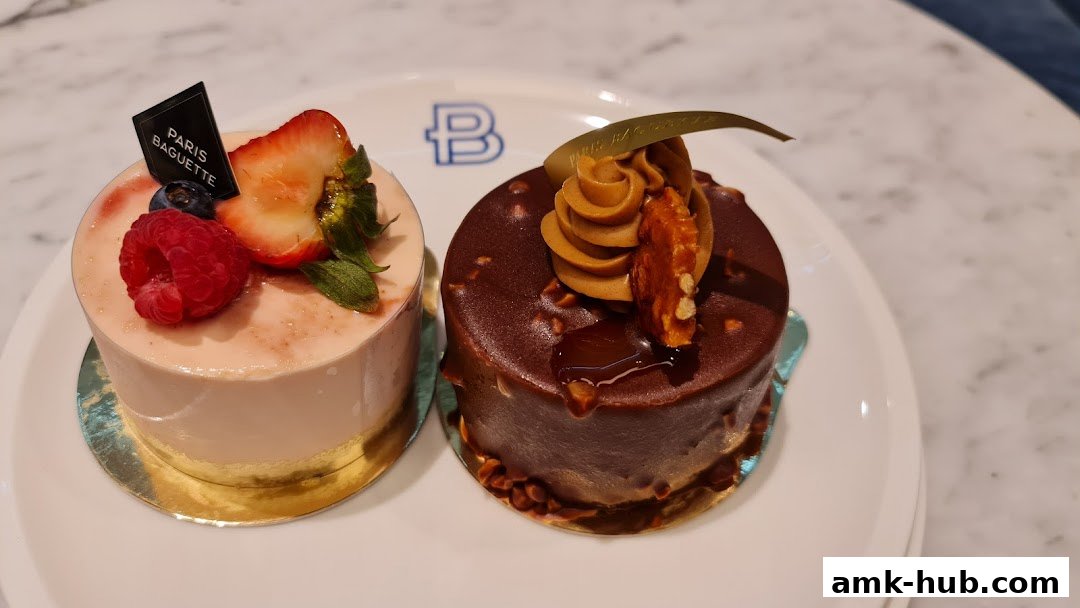 Two beautifully decorated cakes, one with fruit and the other chocolate, are displayed on a white plate.