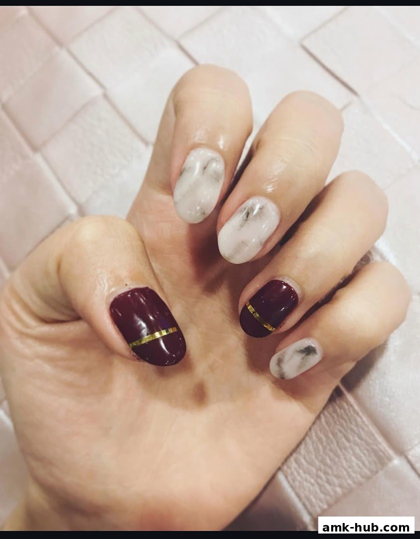 A close-up of a hand with stylish marble and burgundy nails with gold accents.