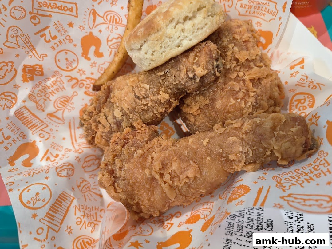 A close-up of Popeyes' signature fried chicken, biscuit, and fries on branded paper.