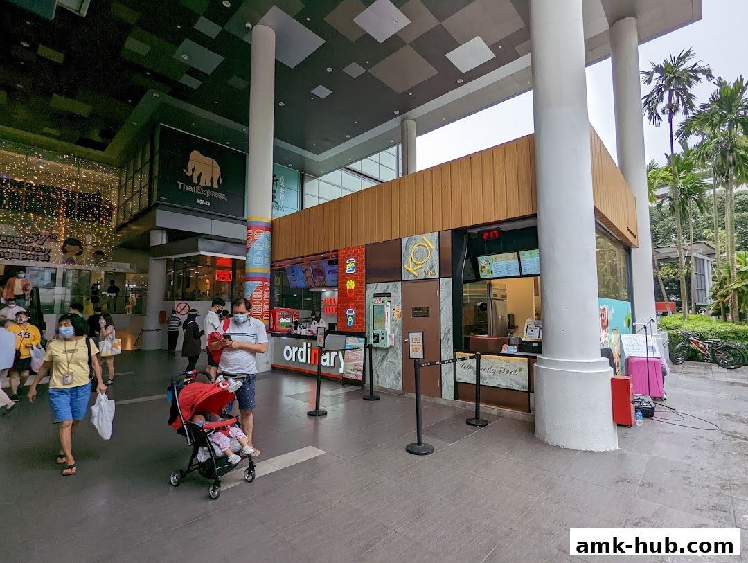 The KOI Thé shop front with customers and a stroller passing by.
