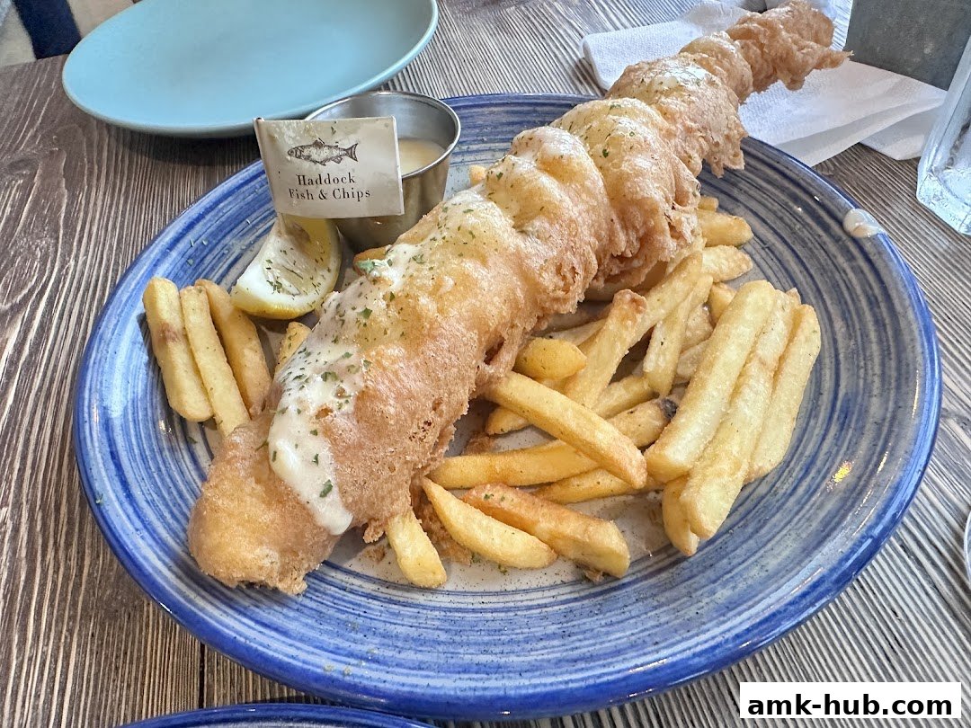 A plate of battered fish and chips with a lemon wedge and sauce.