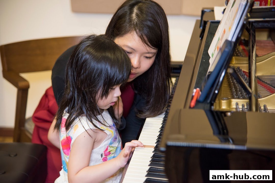 A teacher guides a young child playing a grand piano with sheet music.